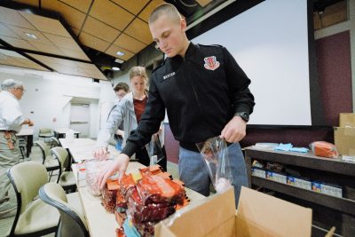 A student in a Corps of Cadets uniform reaches for a koozie to add to a care package for military members.
